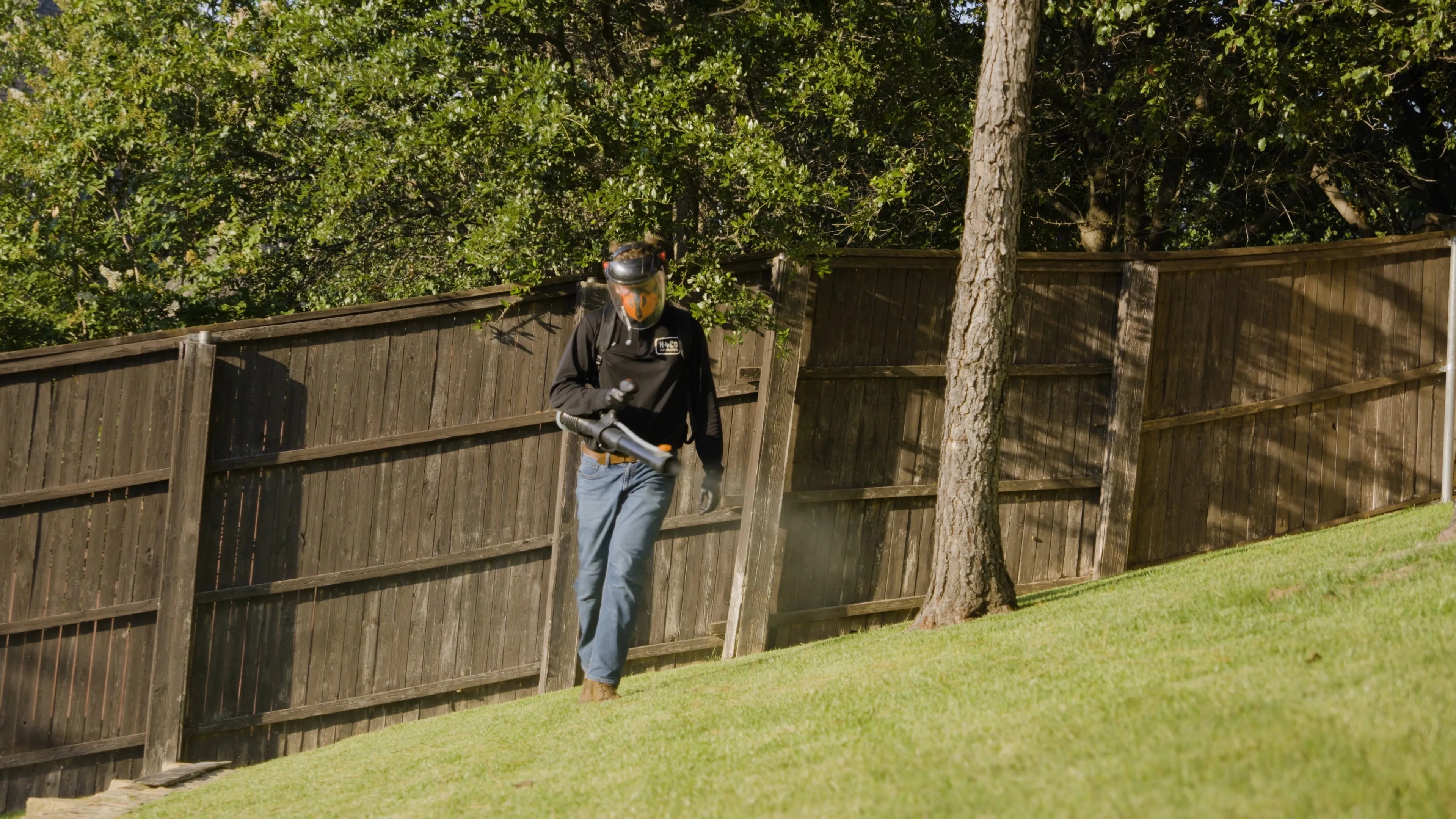 NoCo Pest technician applying backpack barrier spray treatment along fence line to eliminate mosquito resting zones